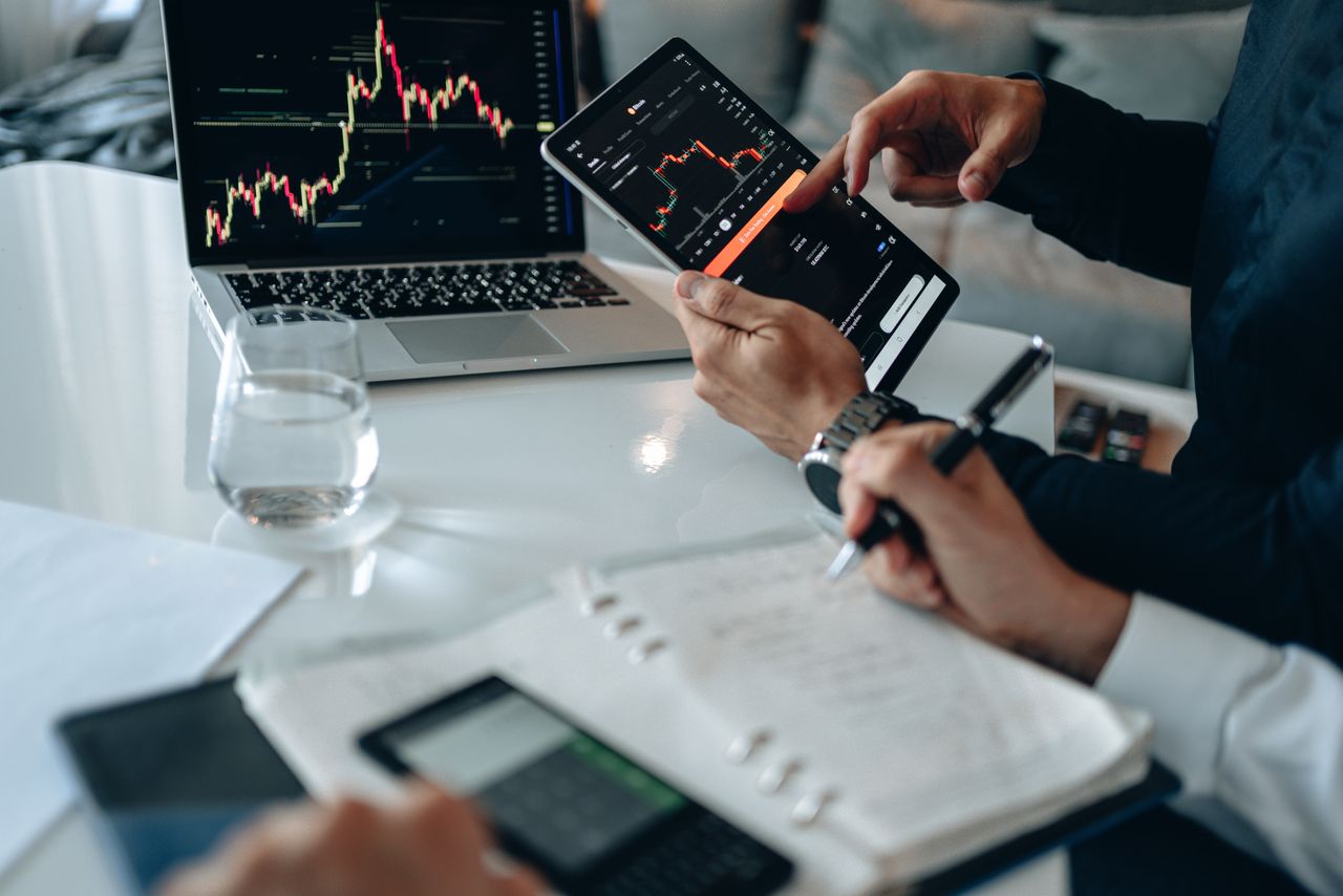Business professionals reviewing financial charts on digital devices in a modern office setting.